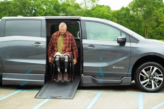 A man in a wheelchair rolling down the ramp of a wheelchair accessible van in a parking lot